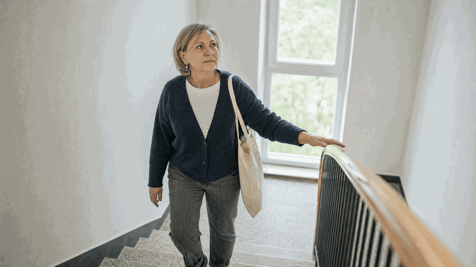 Donna di circa 58 anni sale le scale di casa appoggiando leggermente la mano al corrimano